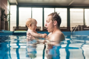 Two family members learn how to swim in private indoor pool with large windows